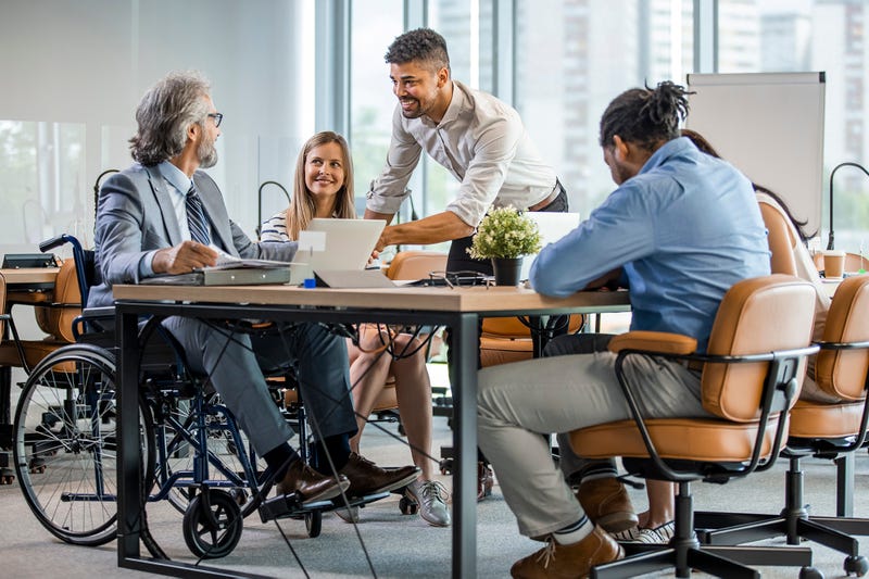 Un groupe diversifié de personnes travaillant dans un bureau lumineux. Un homme est en fauteuil roulant.